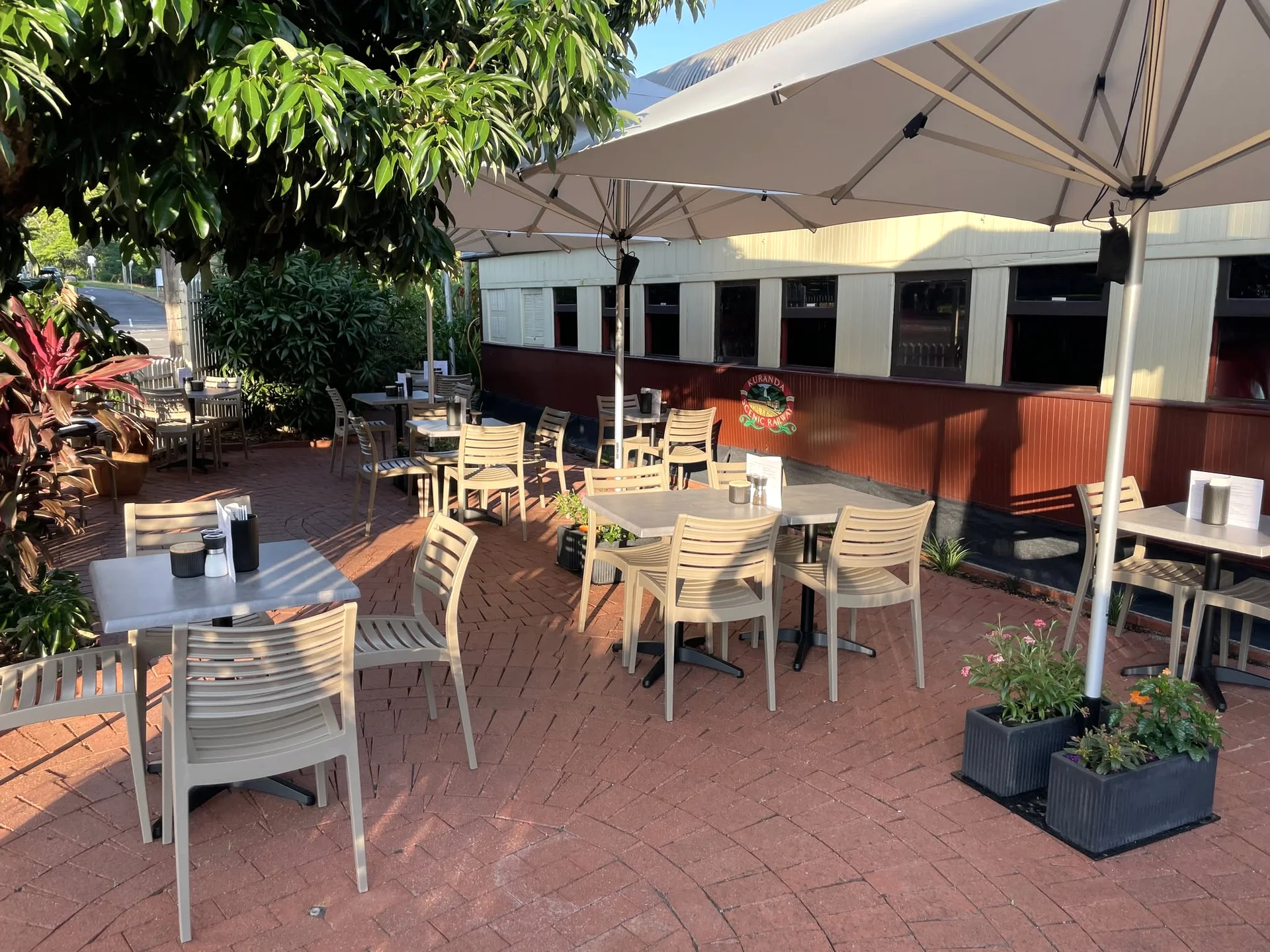 Sunlit tables under cream umbrellas beside the burgundy railway carriage at The Station Freshwater